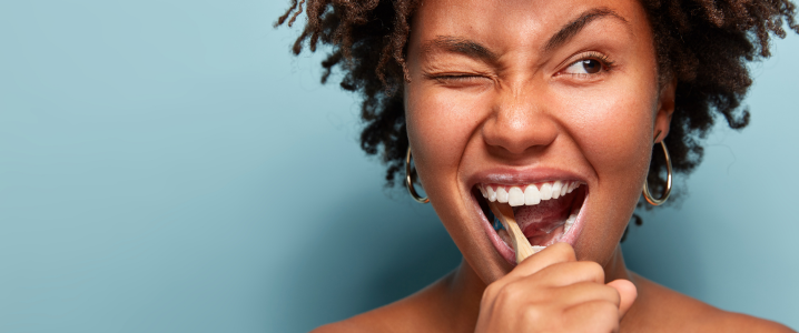 black lady brushing her teeth and smiling, promoting the benefits of following a dental routine to reduce the chance of toothache