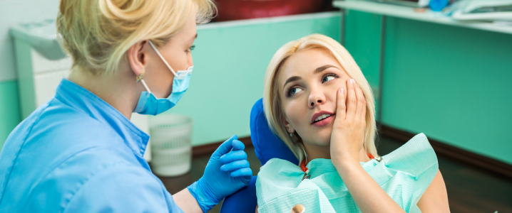 woman holding face in dental pain, female dentist assessing her toothache 