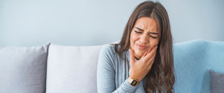 female lady sat on sofa holding her cheek in pain from her toothache