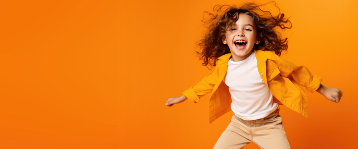 Child smiling and jumping whilst looking at the camera against a bright orange background