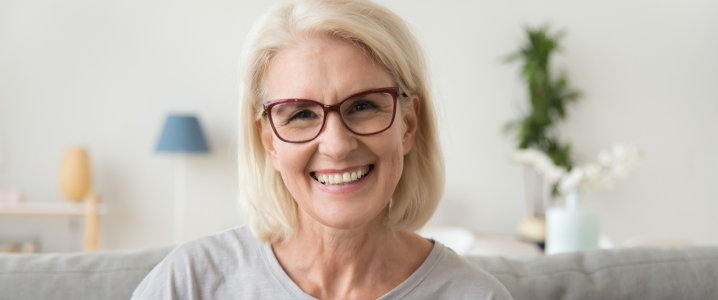 Older woman with glasses smiling at camera with a mouth full of brand new teeth