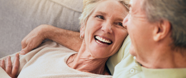 older woman smiling up at husband with a full, white smile