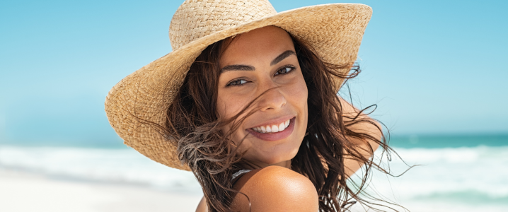 Woman smiling against a beach backdrop with straight white teeth in a sun hat on holiday