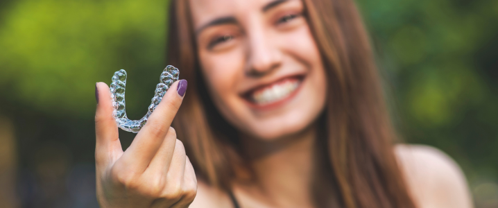 Woman out of focus holding up a clear aligner