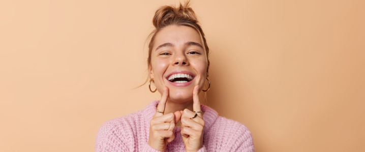 Woman smiling and pointing at straight white teeth against a pale orange background