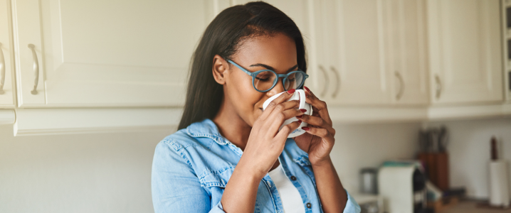 Beautiful black woman sipping cup of coffee in her kitchen