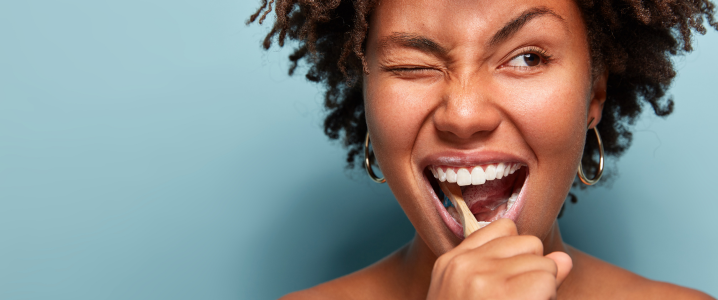 Black woman brushing her teeth against a blue background